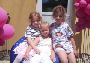 Trzy dziewczynki siedzą na pufie na schodach przedszkola.