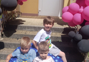 Trzech chłopców siedzi na pufie na schodach przedszkola.