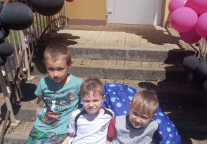 Antek, Bartek, Hubert siedzą na pufie na schodach przedszkola.