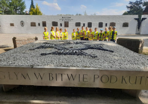 Dzieci stoją wokół płyty upamiętniającej Żołnierzy Poległych w bitwie pod Kutnem. W tle "Mur pamięci" z tablicami pamiątkowymi.