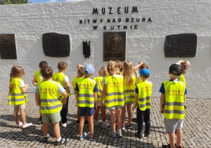 Dzieci oglądają tablice pamiątkowe umieszczone na "Murze pamięci". Na murze znajduje się napis - Muzeum Bitwy nad Bzurą w Kutnie.