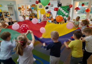 Dzieci trzymają chustę animacyjną i z radości podrzycają do góry balony.
