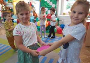 Dwie dziewczynki stoją na dywanie i dopasowują połówki różowej kropki.