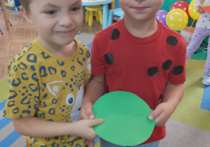 Dwóch chłopców stoi obok siebie. Dzieci dopasowały połówki zielonej kropki.