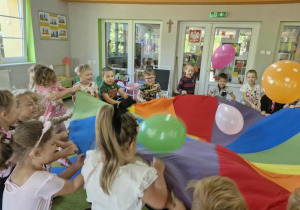 Dzieci stoją przy chuście animacyjnej i podrzucają do góry balony.