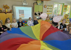 Dzieci trzymają chustę animacyjną i z radością podrzucają do góry balony.