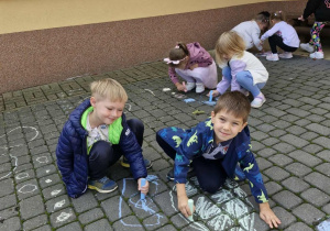 Dwóch chłopców rysuje kolorowe kropki przed wejściem do przedszkola.