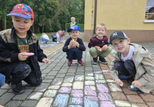 Chłopcy z grupy "Biedronek" kolorowymi kredami malują dużą kropkę przed wejściem do budynku przedszkola.