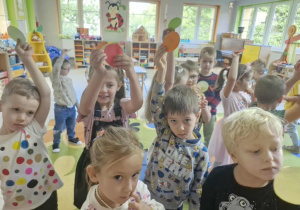 Przedszkolaki trzymają w górze kolorowe kropki z papieru.