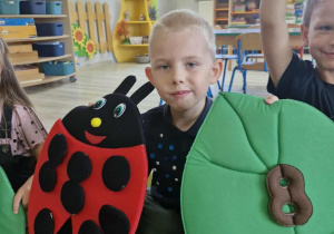 Lucjan trzyma w dłoniach liść z cyfrą 8 i biedronkę, do której przyczepił 8 kropek.