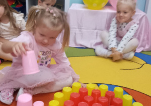 Dzieci siedzą na dywanie i układają z kolorowych kubków kropkę