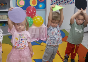 Grupka dzieci stoi na dywanie i trzyma w górze kolorowe kropki.