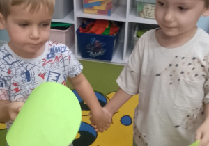 Dwóch chłopców stoi obok siebie trzymając kropki w tym samym kolorze.
