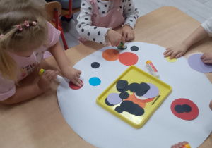 Grupka dzieci siedzi przy stoliku i tworzy kropkowe obrazki.