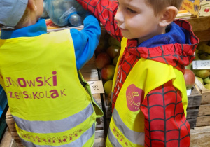 Dwóch chłopców stoi przed ladą w warzywniaku. Mikołaj dokłada do torebki gruszkę.