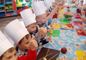 Dzieci siedzą przy wspólnym stole i spożywają swoje owocowe przekąski.