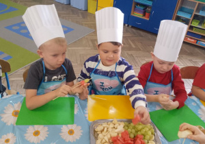 Chłopcy nadziewają na wykałaczki owoce.