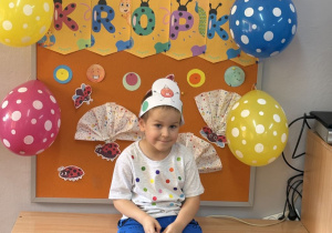 Tymek pozuje na tle gazetki z napisem Dzień Kropki.