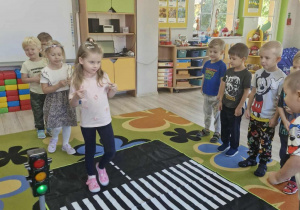 Dzieci z grupy "Biedronek" podczas zabawy "Ruch drogowy" z wykorzystaniem sygnalizatora świetlnego i maty z pasami drogowymi.