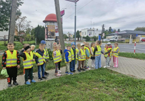 Przedszkolaki stoją w pobliżu skrzyżowania i obserwują ruch drogowy.