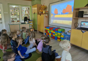 Dzieci z grupy "Biedronek" siedzą na dywanie i oglądają film edukacyjny.