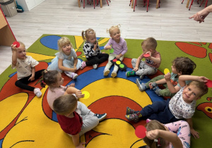 Dzieci siedzą w kole na dywanie trzymając w ręku zielone, żółte oraz czerwone kółka, które miały za zadanie dopasować do sygnalizacji świetlnej.