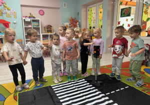 Dzieci podczas zabawy tematycznej czekają, kiedy na sygnalizatorze zapali się zielone światło, aby mogły przejść przez pasy.