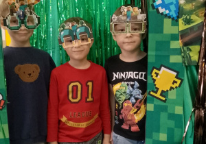 Trójka chłopców w Minecraftowych okularach pozuje do zdjęcia w Minecraftowej fotoramce.