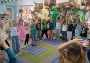 Dzieci ustawione w kole klaszczą nad głowami.