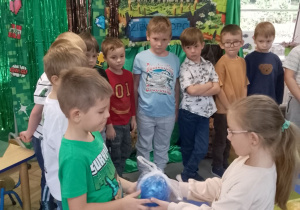 Chłopcy stoją w półkolu na tle dekoracji, Zuzia wręcza Mikołajowi upominek.