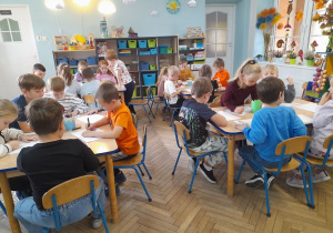 Dzieci siedzą przy stołach i rysują obrazki do wysłuchanych opowieści.