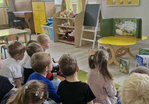Dzieci siedzą na dywanie spoglądając w stronę Teatrzyku Kamishibai.