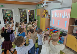 Dzieci tańczą do piosenki z pokazywaniem wyświetlanej na tablicy multimedialnej.