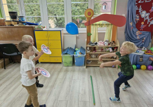 Marcel i Lucjan trzymają w dłoniach tarcze i odbijają balony rzucane przez Karola.
