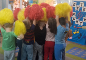 Dzieci stoją w małym kółeczku z pomponami trzymanymi w górze.