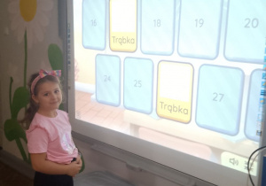 Dziewczynka stoi przed tablicą multimedialną i gra w memory.