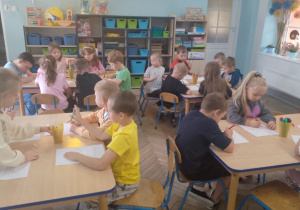 Przedszkolaki siedzą przy stolikach i kolorują obrazki.