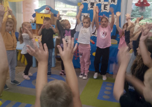 "Słoneczka" stoją w kole z uniesionymi rękami do góry.