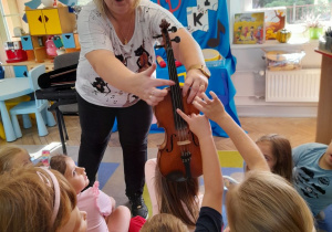 Pani trzyma skrzypce, a dzieci delikatnie dotykają strun.