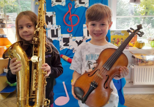 Dwoje dzieci pozuje do zdjęcia z instrumentami muzycznymi. Amanda trzyma saksofon, a Staś skrzypce.