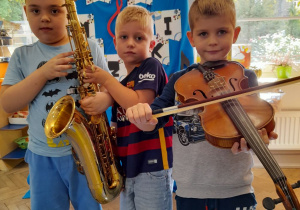 Trzech chłopców pozuje do wspólnego zdjęcia. Wiktor i Jakub trzymają saksofon, a Mikołaj skrzypce.