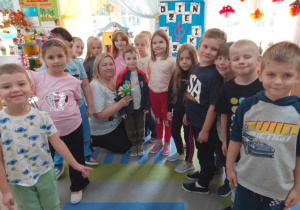 Dzieci razem z mamą Bartka pozują do wspólnego zdjęcia. Pani trzyma bukiecik kwiatków.