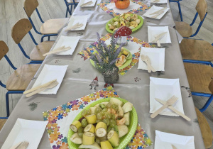 2.Stół przygotowany na zajęcia kulinarne. Na stole widać półmiski w z wybranymi owocami, talerzyki, noże i widelce