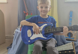 12.Olek siedzi na krześle z gitarą elektryczną w dłoniach. W tle widać dekorację przygotowaną na Dzień muzyki