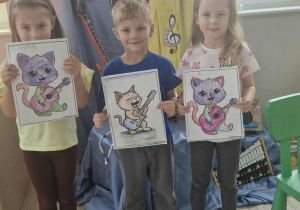 13.Oliwia, Olek i Ola stoją na tle dekoracji i pokazują swoje kolorowanki