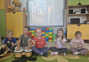 4.Dzieci siedząc na dywanie grają na instrumentach muzycznych