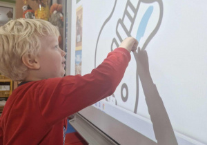 9.Karol na tablicy multimedialnej koloruje szablon gitary