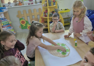 18.Dzieci siedzą przy stoliki i naklejają jabłuszka i koszyczek na biały karton