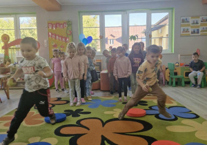 4.Szymek i Staś biegną z jabłkami w dłoniach. W tle widać dzieci ustawione w dwóch rzędach