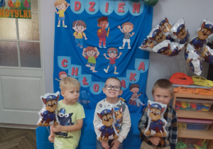 Trzej chłopcy trzymają w ręku balony, na tle dekoracji